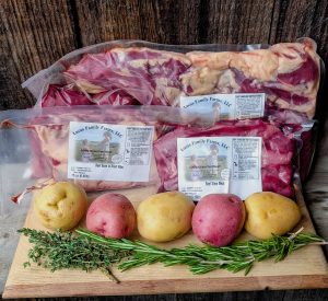 Photo of local meats at Woodstock Farmers' Market. Three cuts of meat from Lucas Family Farm with five potatoes and herbs.