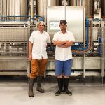 Jasper Hill Farm cheese available at Woodstock Farmers' Market. Image shows two men standing in front of a large piece of equipment used for cheesemaking. 